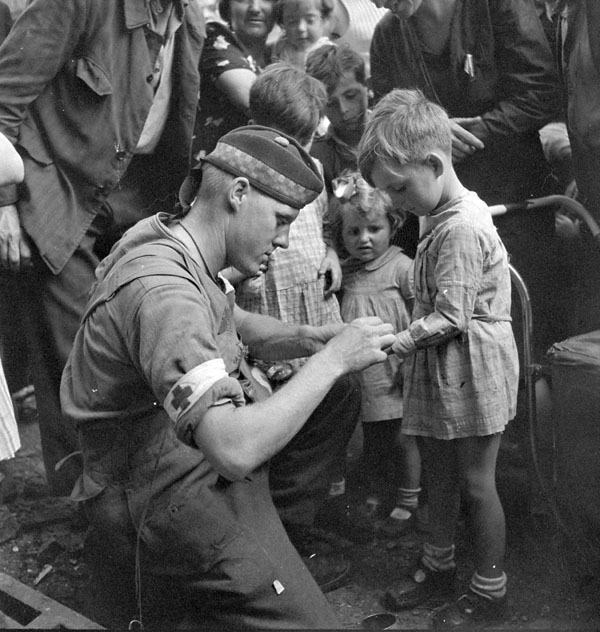 Private G.R. MacDonald of The Toronto Scottish Regiment (M.G.) giving first aid to an injured French boy, Brionne, France, 25 August 1944