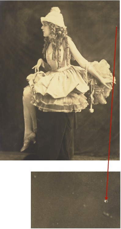 Profil d'une jeune fille assise sur un tabouret, vêtue d'une jupe bouffante. On voit une petite perforation sur la bordure supérieure droite de la photographie. Gros plan d'une petite perforation.