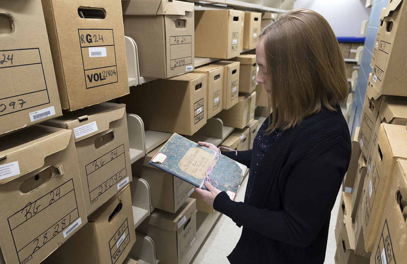 Consultation Clerk Sarah D’Aurelio inspects a ledger in the storage area for archival documents at 395 Wellington Street. Photo: Tom Thompson