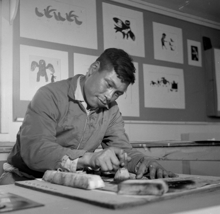 Black and white photo showing Inuit artist making a print with a stencil and a brush.