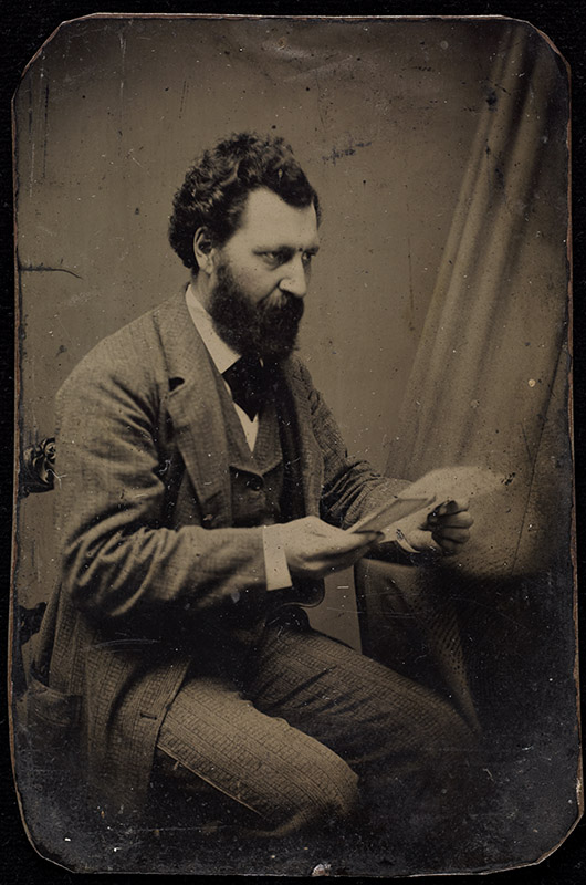Vieille photographie monochrome montrant un homme barbu en complet  assis tenant un morceau de papier