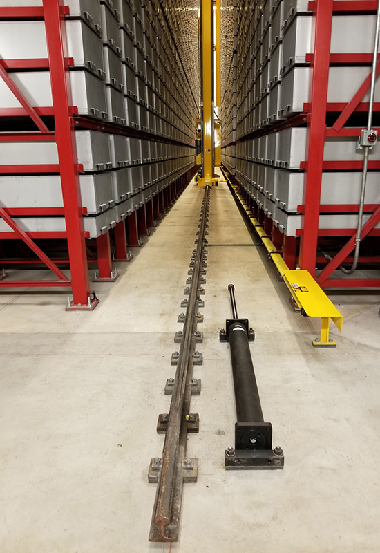 Color photo showing 2 high and deep shelves with metal structure and drawers in the center of which is a freight elevator moving on a rail