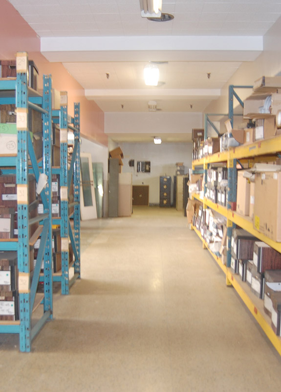 Photo couleur d'un grand entrepôt éclairé montrant 2 rangées d'étagères remplies de boîtes de rangement, séparées par une large allée au milieu