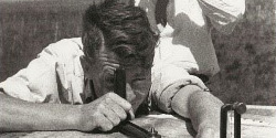 Photo en noir et blanc d'une scène diurne montrant, du devant à l'arrière, un homme appuyé sur une plate-forme numérotée ronde ulitisant un dispositif télescopique rotatif, un homme tenant des jumelles et un panorama forestier