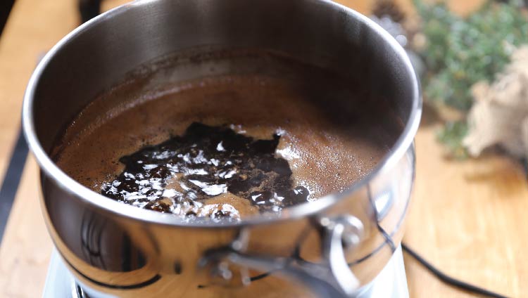 A saucepan of boiling dark coffee on a stove