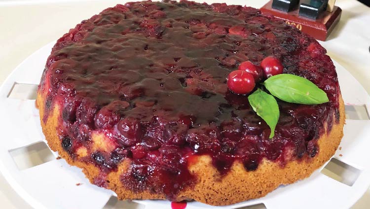 A round, light brown cake topped with red cranberry sauce