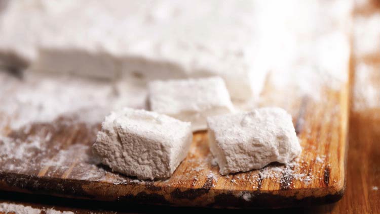 Square marshmallows on a wooden platter, dusted in icing sugar