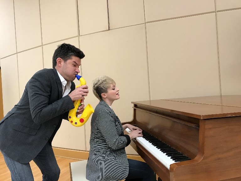 Matt Dusk standing playing a toy saxophone and Barbra Lica seated playing a piano 