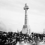 Black and White photograph of a crowd beneath a stone monument with a large Celtic cross.