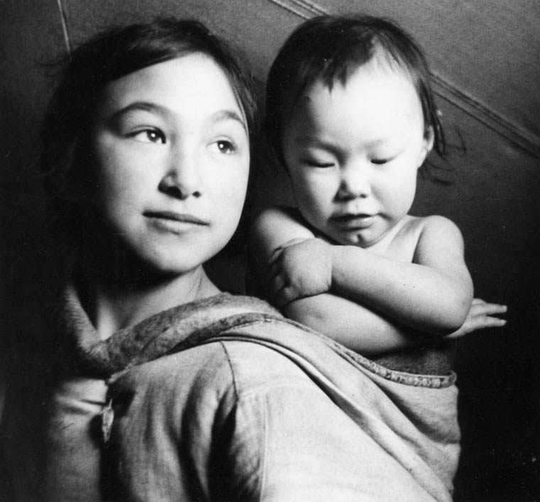 Photo d'une jeune fille inuite portant un enfant dans un porte-bébé, Taloyoak (anciennement SpenceBay), Nunavut, vers 1961