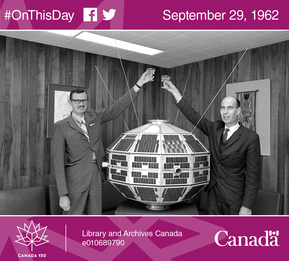Photo of Dr. Leroy Nelms and Dr. John Chapman making a toast beside a model of the Alouette satellite, August 24, 1970