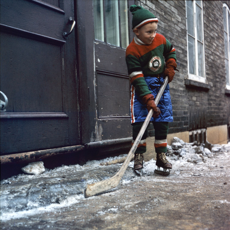 Garçon avec un bâton et des patins de hockey devant une maison, ville de Québec